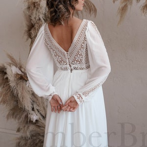 May include: A white wedding dress with long sleeves and a lace bodice. The dress has a deep V-neckline and a button-up back.