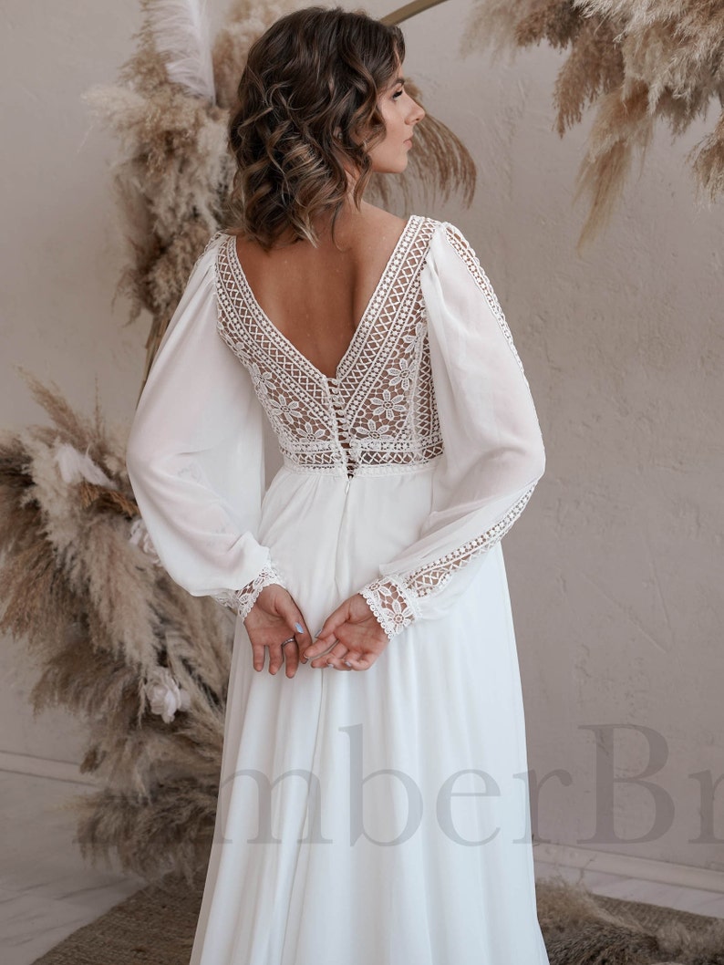 May include: A white wedding dress with long sleeves and a lace bodice. The dress has a deep V-neckline and a button-up back.