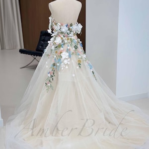 May include: A white tulle wedding dress with a strapless bodice and a floral embroidery design. The dress has a full skirt and a long train.
