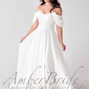May include: A white off-the-shoulder wedding dress with a flowing skirt and a thigh-high slit. The dress features draped sleeves and a fitted bodice. The text "Amber Bride" is visible at the bottom of the dress.