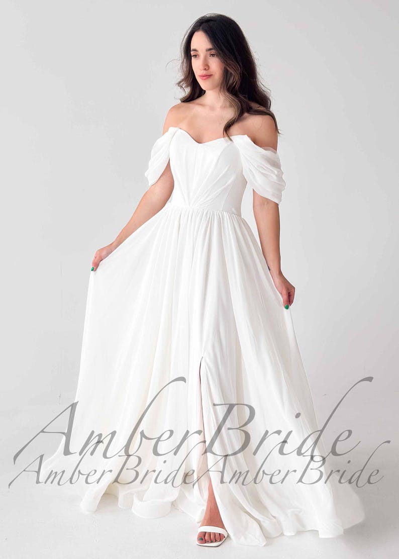 May include: A white off-the-shoulder wedding dress with a flowing skirt and a thigh-high slit. The dress features draped sleeves and a fitted bodice. The text "Amber Bride" is visible at the bottom of the dress.