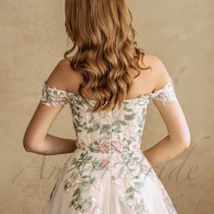 May include: A white off-the-shoulder gown with floral embroidery. The gown has a fitted bodice and a flowing skirt.