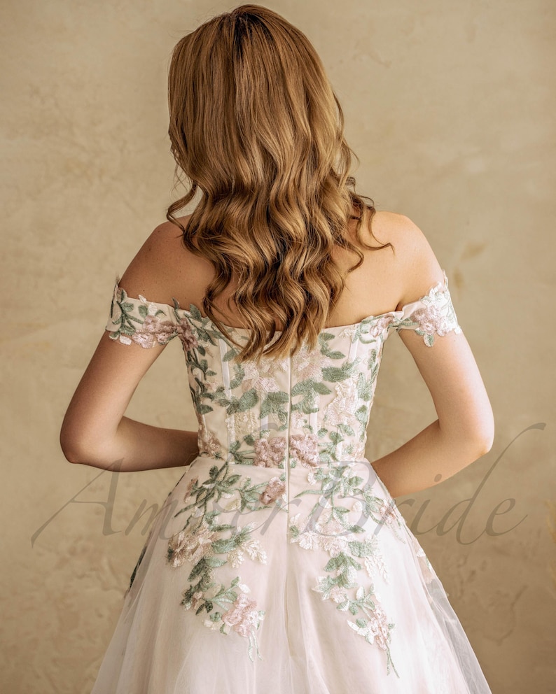 May include: A white off-the-shoulder gown with floral embroidery. The gown has a fitted bodice and a flowing skirt.