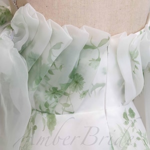 May include: White dress with a green floral print and a ruffled neckline. The dress has a zipper closure in the back.
