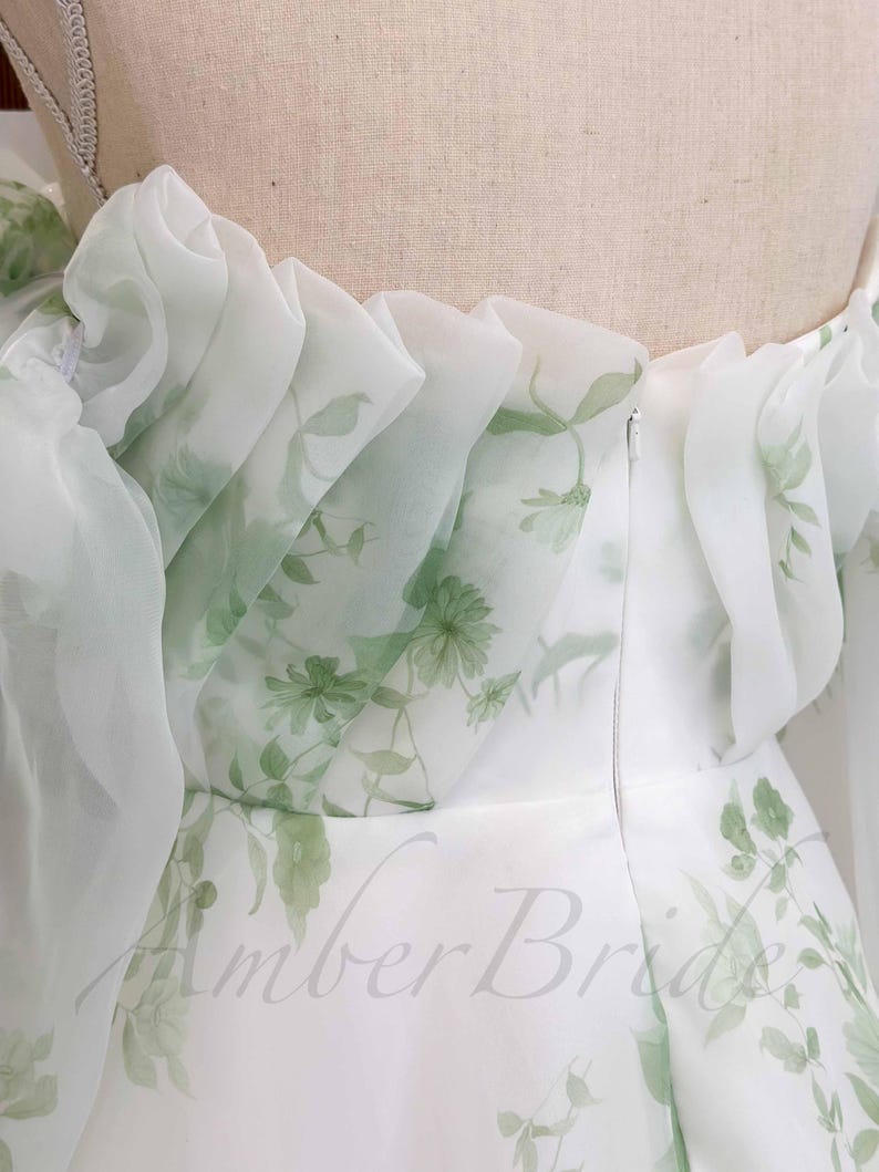 May include: White dress with a green floral print and a ruffled neckline. The dress has a zipper closure in the back.
