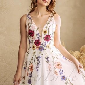May include: A white tulle dress with a plunging neckline and floral embroidery. The embroidery features a variety of colors, including red, pink, yellow, and blue.
