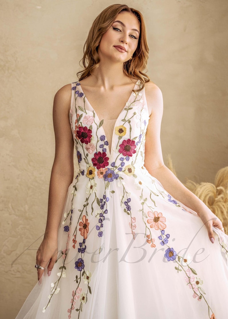 May include: A white tulle dress with a plunging neckline and floral embroidery. The embroidery features a variety of colors, including red, pink, yellow, and blue.