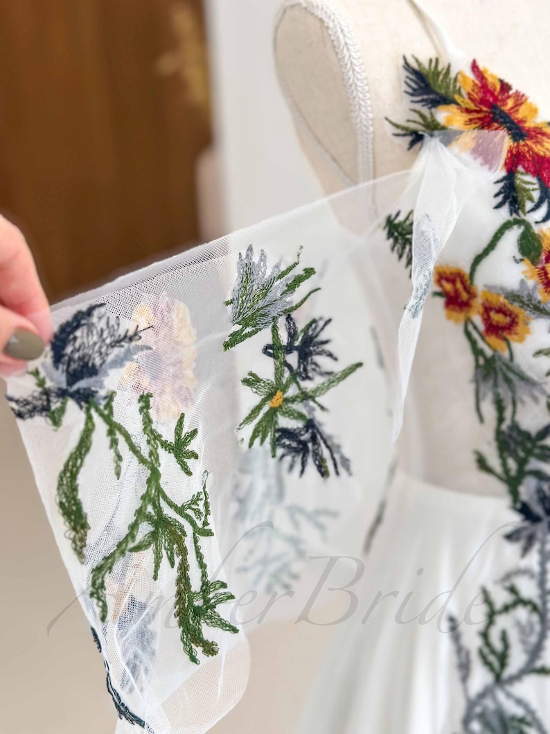 May include: White tulle fabric with embroidered floral designs in shades of green, blue, yellow, and red.