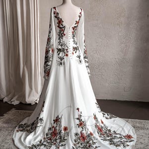 May include: A white maxi dress with long sleeves and a floral print. The dress has a V-neckline and a button-up back.