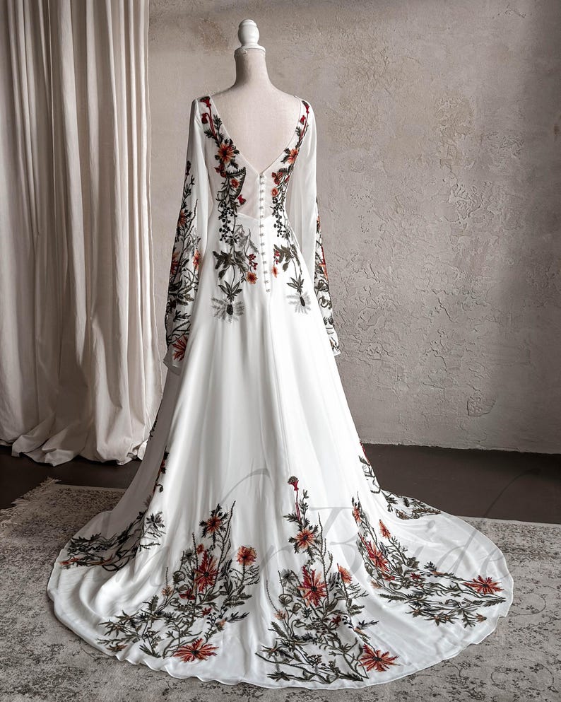 May include: A white maxi dress with long sleeves and a floral print. The dress has a V-neckline and a button-up back.
