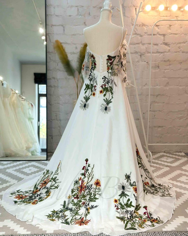 May include: A white wedding dress with a floral pattern. The dress has a sweetheart neckline and a flowing skirt. The floral pattern is in shades of green, yellow, and orange.