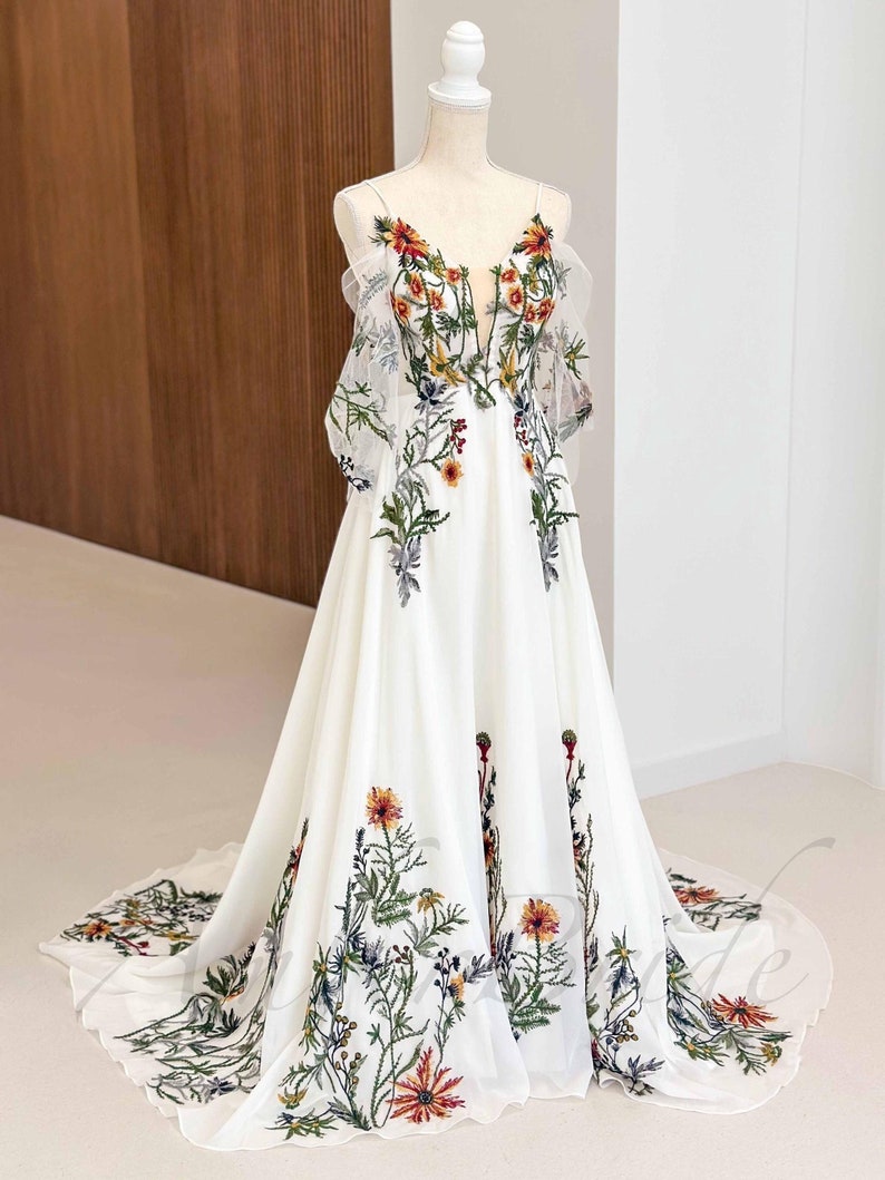 May include: A white maxi dress with a floral print. The dress has a V-neckline and a flowy skirt. The floral print is in shades of red, yellow, green, and blue.