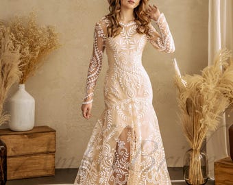 May include: A long-sleeved floor-length dress featuring a nude-colored base layer with intricate white floral and scrollwork embroidery throughout. The garment includes a high neckline, fitted bodice, and a flared skirt with a train.