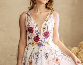 May include: A white tulle dress with a plunging neckline and floral embroidery. The embroidery features a variety of colors, including red, pink, yellow, and blue.