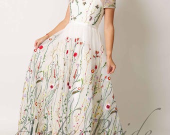Puede incluir: Un vestido maxi blanco con un patrón de bordado floral. El vestido tiene un escote de corazón y mangas cortas. El vestido está hecho de una tela transparente y tiene una falda fluida.