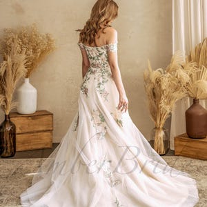 May include: A white off-the-shoulder wedding dress with floral embroidery. The dress has a tulle skirt and a fitted bodice.