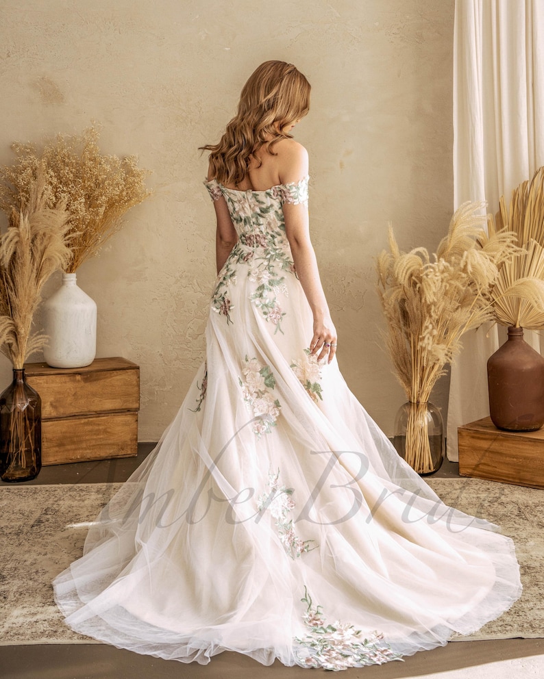 May include: A white off-the-shoulder wedding dress with floral embroidery. The dress has a tulle skirt and a fitted bodice.