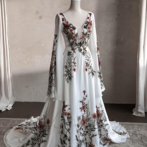 May include: A white maxi dress with long sleeves and a V-neckline. The dress is covered in a floral print with red, orange, and green flowers.