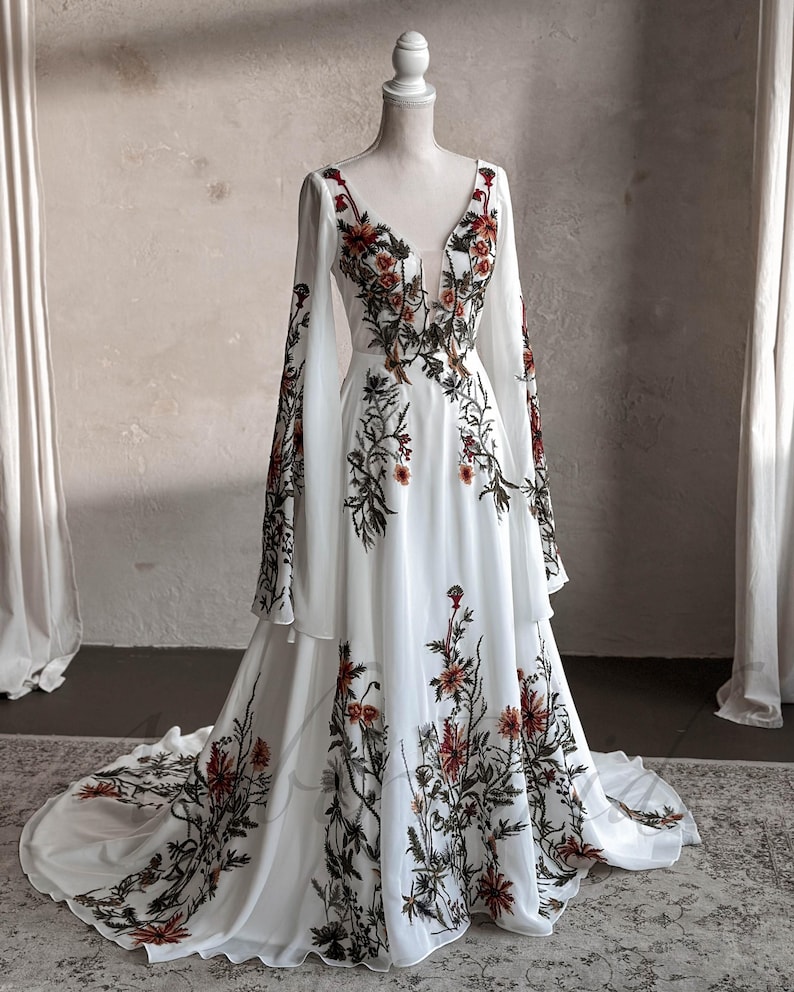May include: A white maxi dress with long sleeves and a V-neckline. The dress is covered in a floral print with red, orange, and green flowers.
