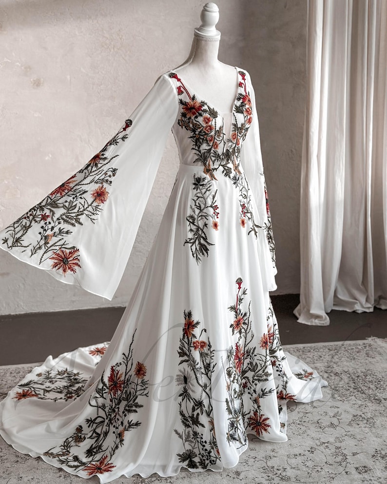 May include: A white maxi dress with long sleeves and a V-neckline. The dress is covered in a floral print with red, orange, and green flowers.