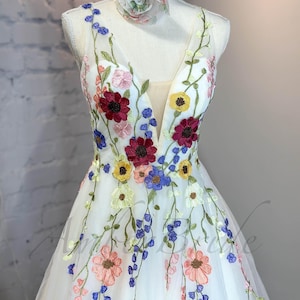 May include: A white tulle dress with a plunging neckline and colorful floral embroidery. The dress has a full skirt and is perfect for a special occasion.