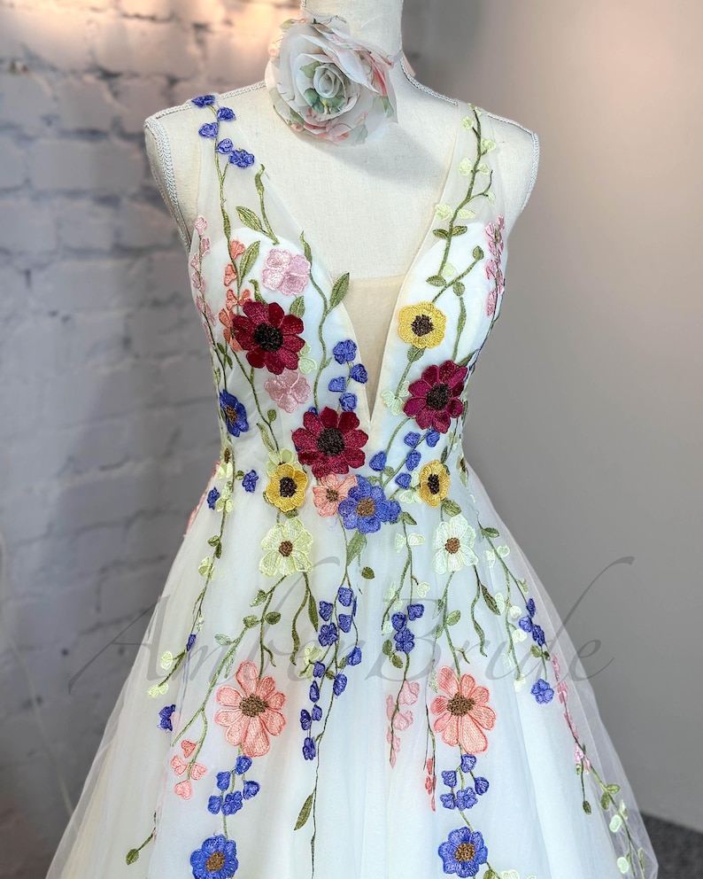 May include: A white tulle dress with a plunging neckline and colorful floral embroidery. The dress has a full skirt and is perfect for a special occasion.