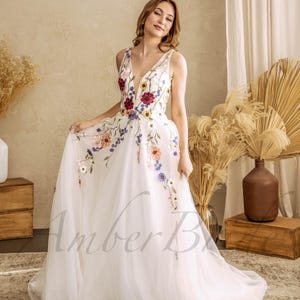 May include: A white tulle wedding dress with a V-neckline and floral embroidery. The dress has a full skirt and a train.