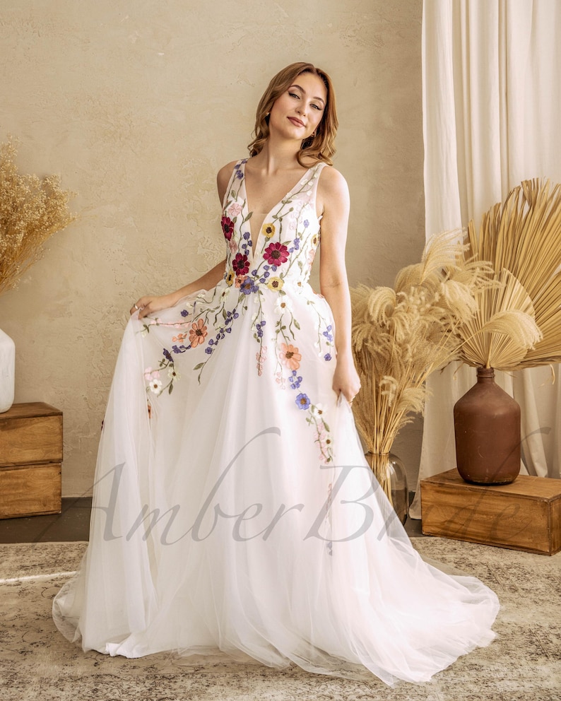 May include: A white tulle wedding dress with a V-neckline and floral embroidery. The dress has a full skirt and a train.