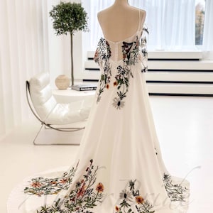 May include: A white maxi dress with a floral print. The dress has a fitted bodice and a flowing skirt. The floral print is in shades of green, orange, and brown.