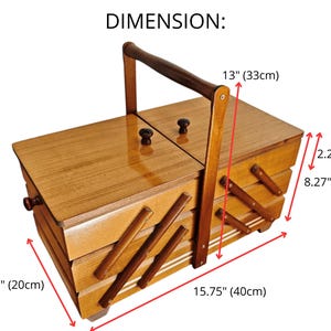 Pu&ograve; includere: Un portacucito in legno con design a sbalzo a pi&ugrave; livelli, dotato di una maniglia centrale e due coperchi superiori con piccoli pomelli. La scatola misura 40 cm di lunghezza, 20 cm di larghezza e 21 cm di altezza, con livelli alti 5,7 cm.
