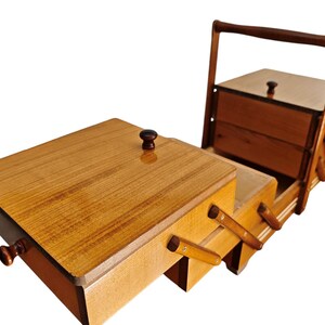 Pu&ograve; includere: Un portacucito in legno con un design a livelli estensibile dotato di scomparti multipli. La scatola presenta una finitura lucida color marrone chiaro, un manico alto e piccoli pomelli marrone scuro sui coperchi. &Egrave; in posizione aperta.