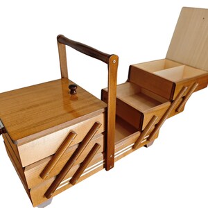 Pu&ograve; includere: Un portacucito in legno con un design a livelli estensibile dotato di molteplici scomparti. La scatola presenta una finitura lucida color marrone chiaro, una maniglia centrale per il trasporto e piccoli pomelli scuri sui coperchi.