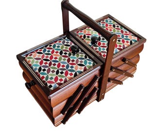 May include: A wooden accordion-style sewing box with a dark brown finish and a central carrying handle. The top features two hinged lids upholstered in a multi-colored fabric with a geometric pattern of red, blue, and green circles and diamonds.