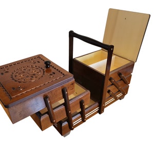 Puede incluir: Una caja de costura de madera con tapa abatible y tres cajones. La caja tiene un dise&ntilde;o tallado en la parte superior y un asa en el lateral.