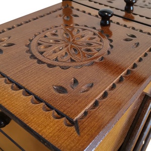 Puede incluir: Una caja de madera con tres cajones, cada uno con un dise&ntilde;o tallado y una perilla. El caj&oacute;n superior tiene un dise&ntilde;o circular con un patr&oacute;n floral.