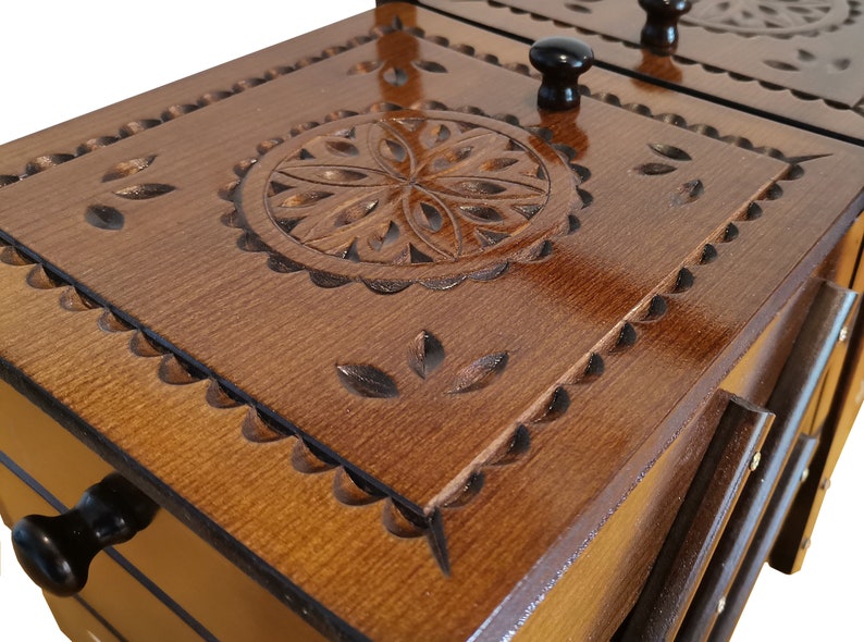 Puede incluir: Una caja de madera con tres cajones, cada uno con un dise&ntilde;o tallado y una perilla. El caj&oacute;n superior tiene un dise&ntilde;o circular con un patr&oacute;n floral.