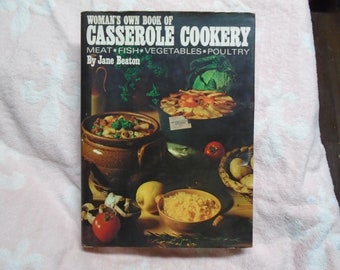 May include: A vintage cookbook titled "Woman's Own Book of Casserole Cookery: Meat, Fish, Vegetables, Poultry" by Jane Beaton. The cover features a photo of a casserole dish with a brown lid and a casserole dish with a black lid, both filled with food. There are also various vegetables and other food items on the cover.