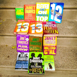 May include: A selection of Janet Evanovich novels, including "Hard Eight," "Eleven on Top," and "Twelve Sharp." The books are displayed on concrete steps, with a range of vibrant book cover designs.