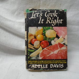 Op de afbeelding: Een vintage kookboek getiteld "Let's Cook It Right" door Adella Davis. De omslag toont een kleurrijke illustratie van verschillende voedingsmiddelen, waaronder vlees, groenten en fruit.