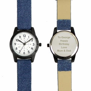 May include: A black wristwatch with a white face and blue canvas band. The watch face displays black numerals and hands. The back of the watch has the inscription "To George Happy Birthday Love Mum & Dad."