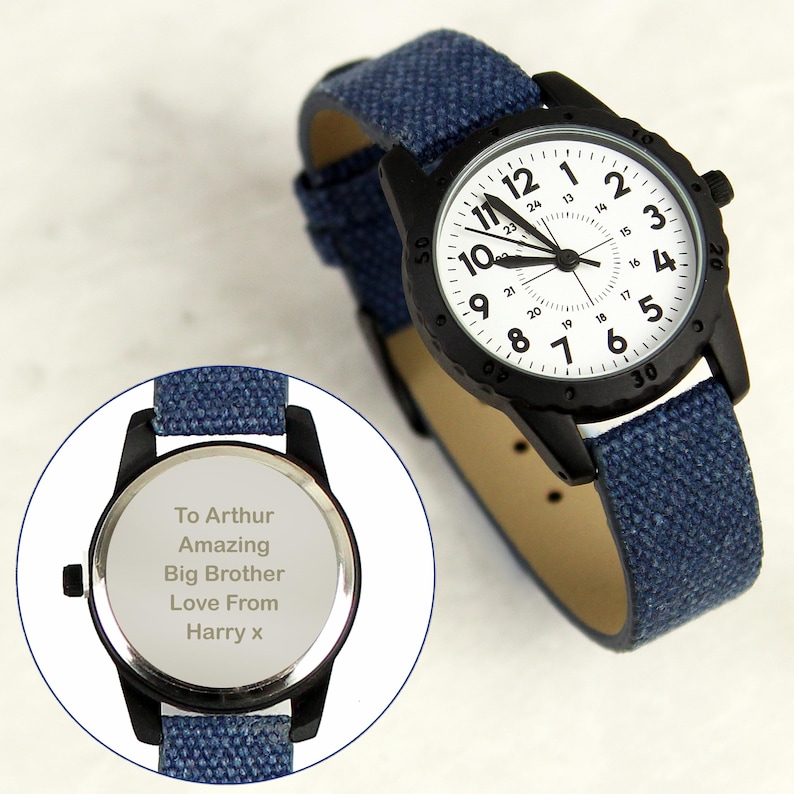 May include: A black wristwatch with a white face and blue denim strap. The watch face has black numerals and hands. The back of the watch has engraved text that reads: "To Arthur Amazing Big Brother Love From Harry x."