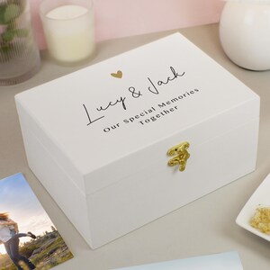 May include: A white wooden keepsake box with gold hardware. The lid features the text "Lucy & Jack" with a gold heart and the words "Our Special Memories Together". The box is closed and sits on a light surface.