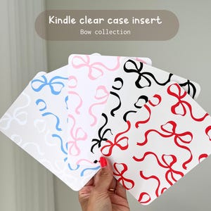 May include: Four different designs of Kindle clear case inserts with a bow pattern. The designs are white with blue bows, white with pink bows, white with black bows, and white with red bows. The text "Kindle clear case insert" and "Bow collection" is visible at the top of the image.