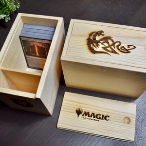 May include: Two wooden boxes for storing Magic: The Gathering cards. One box has a dragon design burned into the lid. The other box has a Magic: The Gathering logo on the lid.