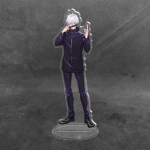May include: An acrylic standee featuring an anime character with white hair, wearing a high-collared dark purple jacket and matching trousers. The character is posed with one hand near their face, standing on a clear circular base.