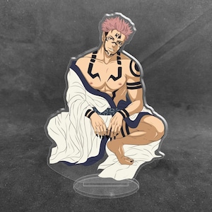 May include: An acrylic standee featuring a character with pink hair, dark facial markings, and a muscular build. The character is shirtless, wearing a white robe with dark blue trim, and is depicted in a seated pose with dark fingernails.