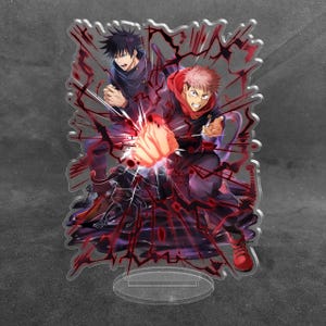 May include: A clear acrylic standee featuring two anime characters in dynamic poses. One character has spiky black hair and a dark uniform, while the other has pink hair, a red hooded jacket, and a glowing fist surrounded by dark red energy effects.