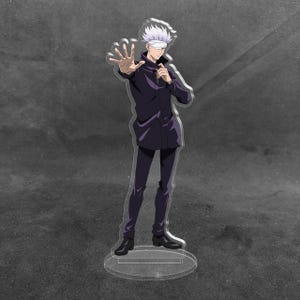 May include: A clear acrylic standee featuring an anime character with spiky white hair and a white blindfold over their eyes. The character wears a dark purple high-collared jacket and matching trousers, standing with one hand extended forward.