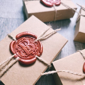 May include: Three small, brown cardboard boxes with twine tied around them. Each box has a red wax seal with a letter 'B' embossed in the centre.