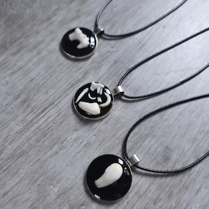 Puede incluir: Tres collares con colgantes negros y plateados con dise&ntilde;os blancos en forma de hueso. Cada colgante es redondo, con fondo negro y borde plateado. Los collares tienen cordones negros.